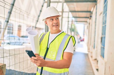 Orta yaşlı mimar akıllı telefon kullanıyor ve şehrin planlarını tutuyor..