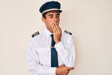 Uçak pilotu üniforması giyen genç İspanyol adam ağzıyla esnemekten sıkılmış. Huzursuz ve uykulu.. 