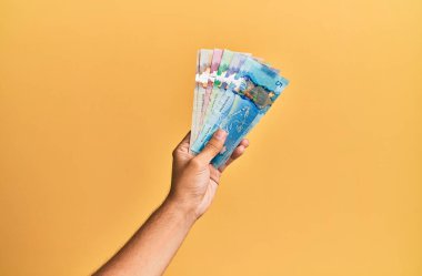 İzole edilmiş sarı arka planda Kanada doları tutan İspanyol bir adamın eli..