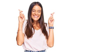 Latin kökenli genç bir kadın, günlük beyaz tişörtler giyip umut ve gözlerin kapalı bir şekilde gülümseyerek el sallıyor. Şans ve batıl inançlar. 