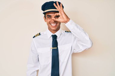 Uçak pilotu üniforması giyen genç İspanyol adam el hareketleriyle gülümsüyor ve mutlu yüzüyle parmaklarının arasından bakıyor.. 