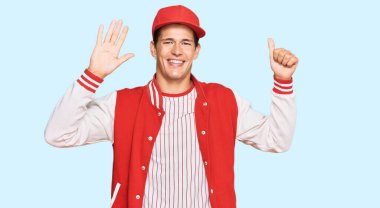 Beyzbol üniforması giyen yakışıklı beyaz adam altı numarayı gösterip işaret ederken kendinden emin ve mutlu bir şekilde gülümsüyor.. 