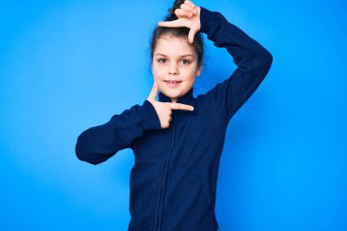 Gündelik kıyafetler giyen sevimli İspanyol çocuk gülümseyerek elleri ve parmakları gülen yüzle çerçeve yapıyor. yaratıcılık ve fotoğrafçılık kavramı. 