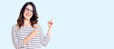 Güzel, genç, esmer bir kadın. Günlük kıyafetler ve gözlük takıyor. Gülümsüyor ve kameraya bakıyor.. 