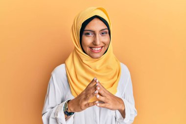 Geleneksel İslami başörtüsü takan genç esmer Arap kadın ellerini birleştirip gülümseyerek gevşemiş ve neşeli olmasını diliyordu. Başarı ve iyimserlik 