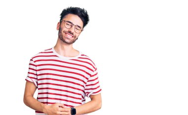 Latin asıllı genç adam ellerinin birleştiği günlük kıyafetler giyiyor ve gülümseyerek gevşemiş ve neşeli gülümsüyor. Başarı ve iyimserlik 