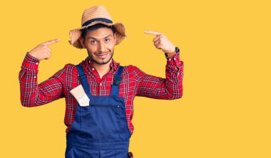 Yakışıklı Latin Amerikalı, giyimli, tamirci üniforması giyen, gülümseyen, iki eliyle başını gösteren, harika bir fikir veya düşünce, iyi bir hafıza. 