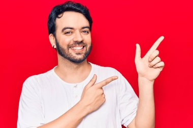 Gündelik kıyafetler giyen genç İspanyol adam gülümseyip kameraya bakıyor ve iki eliyle ve parmaklarıyla kenarı işaret ediyor.. 