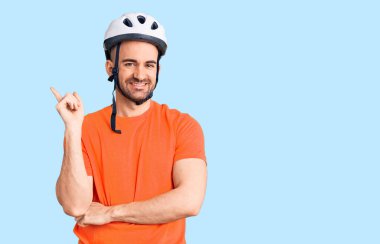 Bisiklet kaskı takan yakışıklı genç adam gülümsüyor. 
