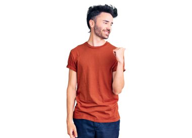 Gündelik kıyafetler giyen, gülümseyen, gülümseyen ve başparmağıyla yan tarafı gösteren İspanyol genç adam.. 