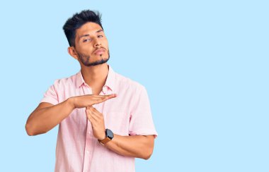 Yakışıklı Latin Amerikalı sıradan bir yaz tişörtü giymiş. El kol hareketi yapıyor, hayal kırıklığına uğramış ve ciddi bir yüz ifadesi takınıyor. 