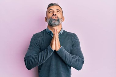 Orta yaşlı yakışıklı bir adam gündelik giysiler giyiyor. Elleriyle yalvarıyor ve dua ediyor. Yüzünde umut ifadesi var. Yalvarıyor. 