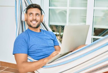 Genç İspanyol adam terastaki hamakta dizüstü bilgisayar ve kulaklık kullanarak rahatça çalışıyordu..