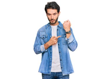 Gündelik kıyafetler giyen genç İspanyol adam saati, sabırsızlığı ve rahat bir ifadeyle kameraya bakmayı işaret ediyor. 