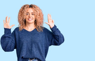 Kıvırcık saçlı, sıradan bir süveter giyen genç sarışın kadın dokuz numaralı parmaklarıyla işaret ederken kendinden emin ve mutlu bir şekilde gülümsüyor.. 