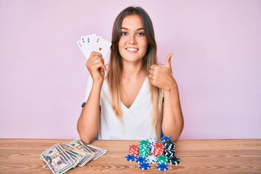 Güzel beyaz kadın poker oynuyor mutlu ve olumlu gülümsüyor, başparmağıyla mükemmel ve onay işareti yapıyor. 