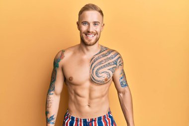 Yüzünde mutlu ve serin bir gülümseme olan mayosuz mayo giyen genç beyaz bir adam. şanslı kişi. 