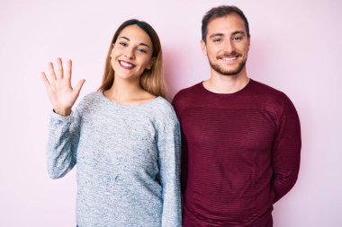 Güzel bir çift gündelik giysiler giyer ve mutlu bir şekilde gülümserken beş numarayı işaret eder.. 