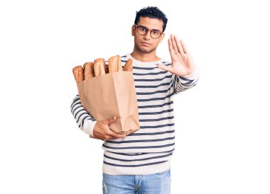 İspanyol asıllı yakışıklı genç adam elinde bir kese kağıdıyla elinde ekmekle dur işareti yapıyor ciddi ve kendinden emin bir ifadeyle savunma hareketi yapıyor. 