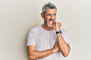 Orta yaşlı, gri saçlı, günlük kıyafetler giyen, gergin ve elleri ağızda olan, tırnaklarını yiyen bir adam. anksiyete. 