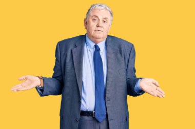 İş ceketi giyen yaşlı, kır saçlı, kafası karışık ve kolları açık, hiçbir fikri olmayan bir adam.. 