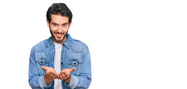 Elleri avuçlarında gülümseyen ya da el hareketi yapan gündelik kıyafetler giyen İspanyol genç bir adam. Bekleme ve koruma 