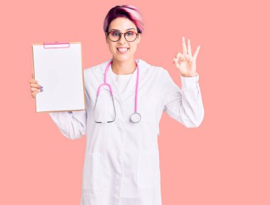 Pembe saçlı, doktor steteskobu takan genç bir kadın elinde tıbbi raporla pano tutuyor. Parmaklarıyla imza atıyor, gülümsüyor. 