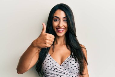 Güzel İspanyol kadın günlük kıyafetler giyiyor mutlu ve pozitif gülümsüyor, başparmağıyla mükemmel ve onay işareti yapıyor. 