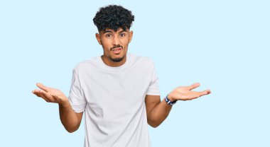 Gündelik beyaz tişört giyen genç bir Arap. Hiçbir fikri olmayan, kolları açık, hiçbir fikri olmayan bir adam.. 