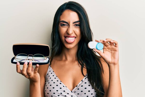 Красивая латиноамериканка, держащая очки и контактные линзы, торчащие языком, довольна смешным выражением лица.. 