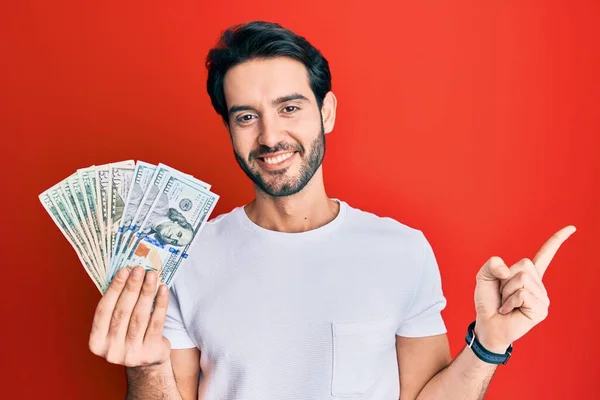 Ung Latinamerikan Man Håller Dollar Ler Glad Pekar Med Hand — Stockfoto