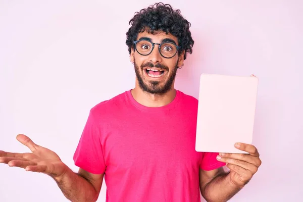 ハンサムな若いです男とともに巻き毛とクマ読書幸せな笑顔と勝者の表現で達成を祝う本を持ち上げ手 — ストック写真