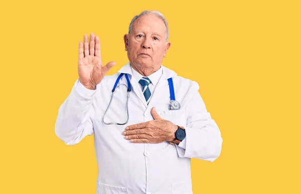 Senior handsome grey-haired man wearing doctor coat and stethoscope swearing with hand on chest and open palm, making a loyalty promise oath