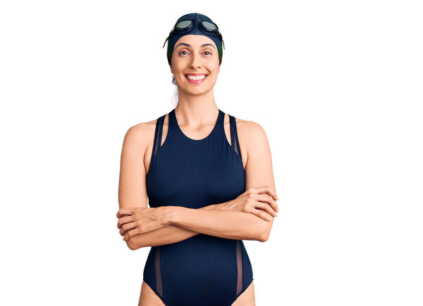 Young beautiful hispanic woman wearing swimwear and swimmer glasses happy face smiling with crossed arms looking at the camera. positive person. 