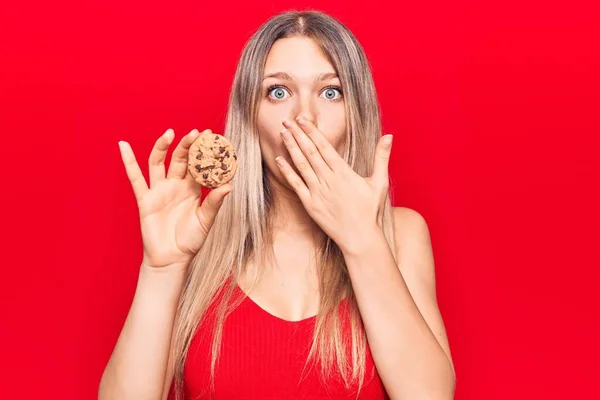 若い美しいブロンドの女性は 手で口をカバークッキーを保持します ショックを受け 間違いを恐れて 驚きの表情 — ストック写真