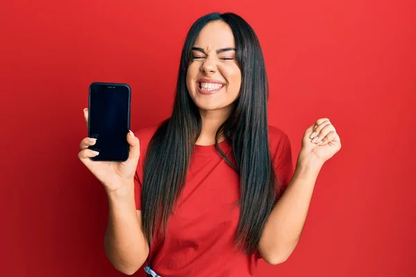 Jovem Bela Menina Hispânica Segurando Smartphone Mostrando Tela Gritando Orgulhoso — Fotografia de Stock