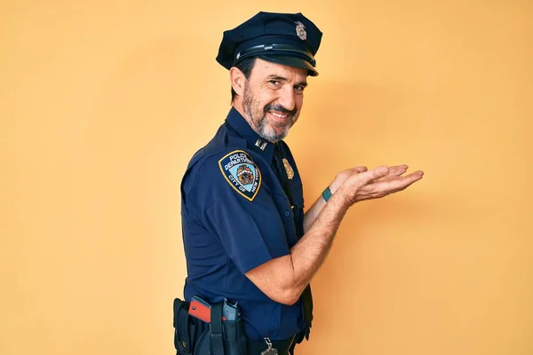 Middle age hispanic man wearing police uniform pointing aside with hands open palms showing copy space, presenting advertisement smiling excited happy