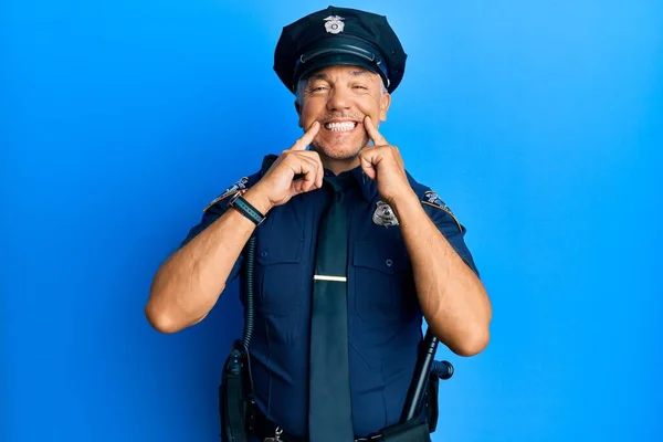 Handsome middle age mature man wearing police uniform smiling with open mouth, fingers pointing and forcing cheerful smile
