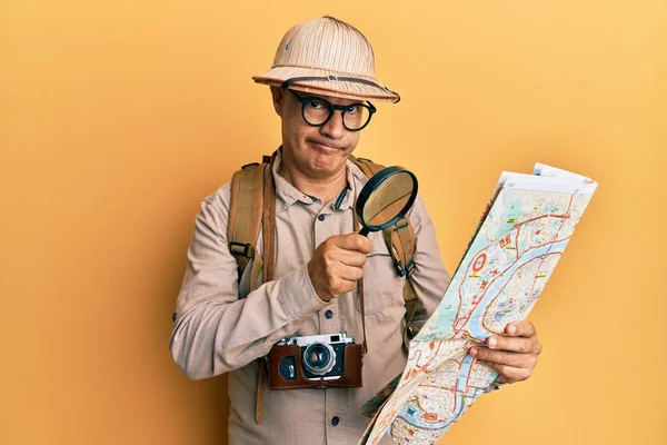地図上で虫眼鏡を保持探検家の帽子をかぶっている中年のはげ男は懐疑的で緊張しており 問題のために動揺して眉をひそめています 否定的な人 — ストック写真