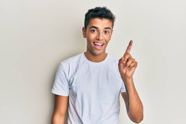 Genç, yakışıklı, Afro-Amerikalı, günlük beyaz tişört giyen, bir fikir veya soruyla gülümseyen, mutlu yüzlü, bir numara. 