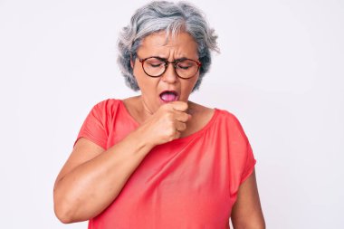 Yaşlı Latin asıllı, gri saçlı, günlük kıyafetler ve gözlük takan, kendini kötü hisseden ve soğuk algınlığı veya bronşitin belirtisi olarak öksüren bir kadın. sağlık hizmeti kavramı. 