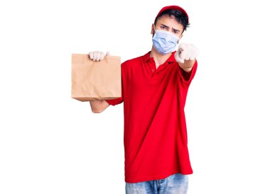 Teslimat üniforması giyen genç İspanyol bir adam ve elinde bir kese kâğıdıyla kamerayı ve seni işaret eden kendine güveni tam bir jest. 