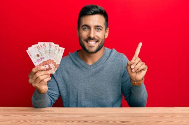 Yakışıklı İspanyol adam Kolombiya pezosu tutuyor. Gülümsüyor. Elleri ve parmakları yana doğru uzanıyor. 