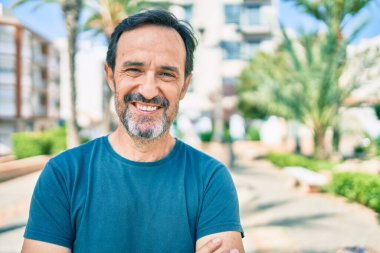 Orta yaşlı, sakallı, açık havada mutlu gülümseyen bir adam.