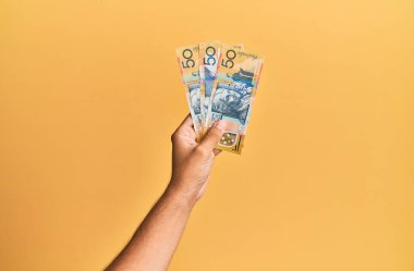 Avustralyalı 50 dolarlık banknotları izole edilmiş sarı arka planda tutan İspanyol adamın eli..