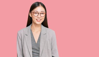 İş elbiseleri giyen genç Çinli kadın pozitif ve mutlu görünüyor. Dişlerini gösteren bir gülümsemeyle ayakta duruyor ve gülümsüyor. 