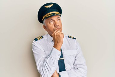 Orta yaşlı, yakışıklı, uçak pilotu üniforması giyen, elleri çenesinde soru soran, düşünceli bir adam. Düşünceli bir yüzle gülümsüyor. şüphe kavramı. 