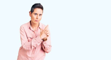 Kısa saçlı, günlük kıyafetler giyen, el hareketleriyle sembolik silah tutan, cinayet silahlarıyla oynayan, sinirli yüzlü genç bir kadın. 