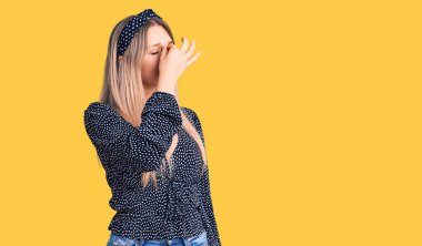 Genç, güzel, sarışın, günlük kıyafetler giyen, burnu ve gözleri ovuşturmaktan yorgun, yorgunluk ve baş ağrısı çeken bir kadın. Stres ve hüsran kavramı. 