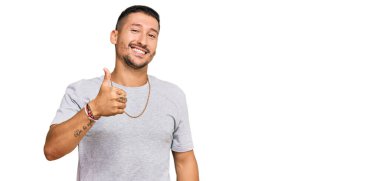 90 'ların tarzında dövmeleri olan yakışıklı bir adam mutlu bir el hareketi yapıyor. Kameraya bakıp başarıyı gösteren ifade. 